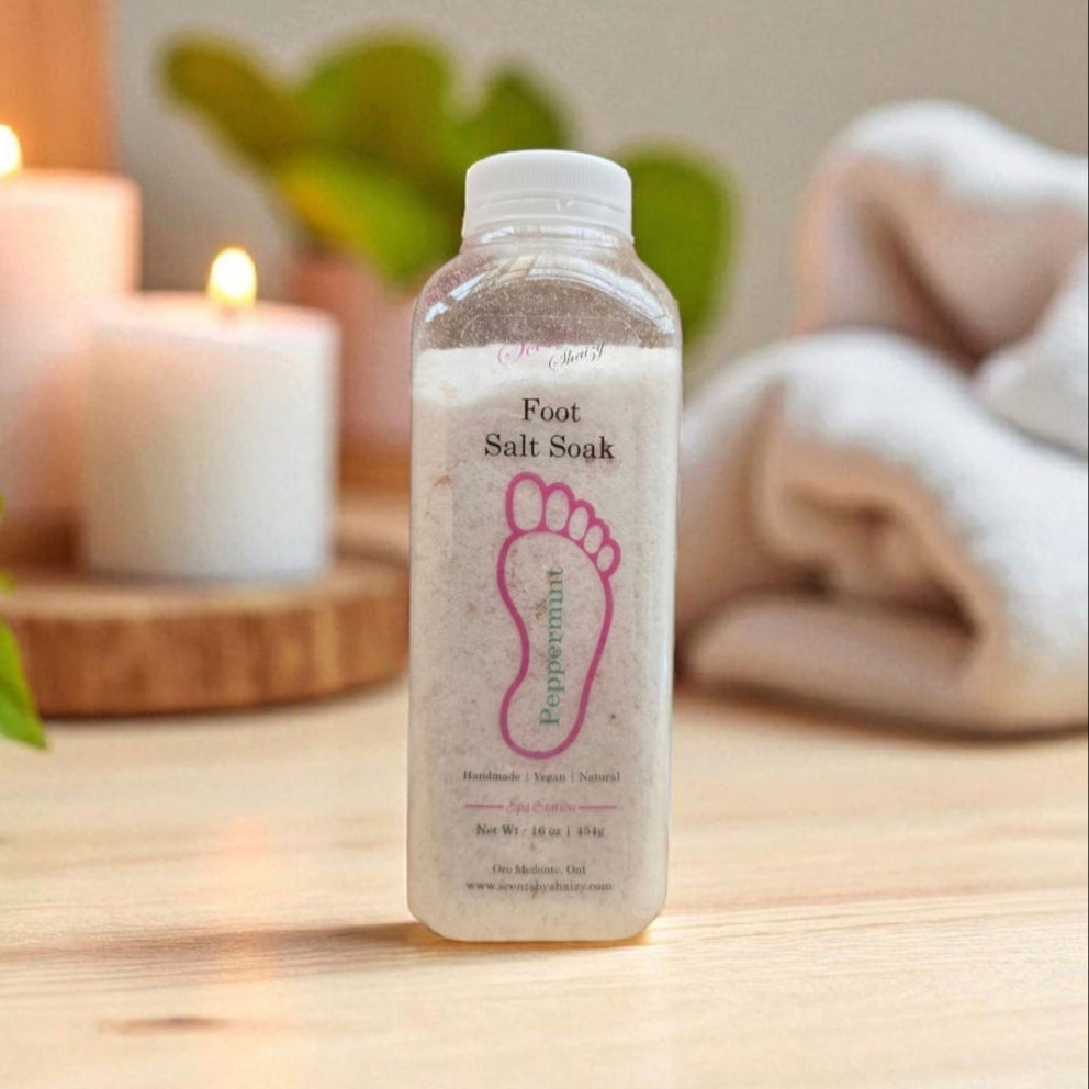 Foot salt soak bottle on a wooden surface with candles and a towel in the background