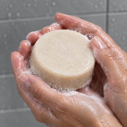 Cream shampoo bar held between wet hands with a little lather